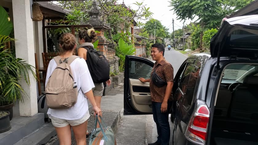 A private driver waiting beside a car at a Bali pickup point