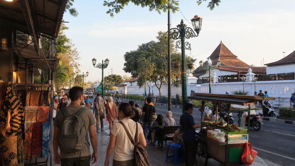 A Yogyakarta street scene with batik stalls, food carts and people walking