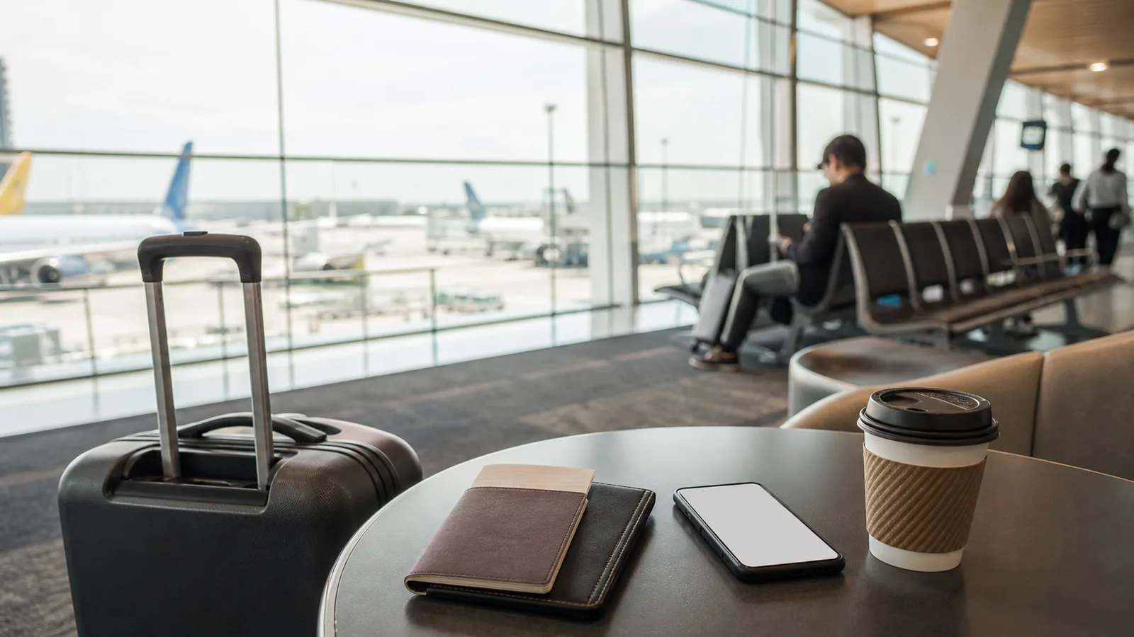 Carry-on suitcase, phone and coffee in a Jakarta airport waiting area